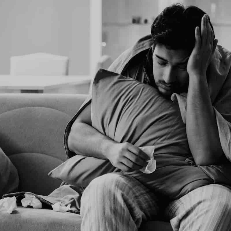 Hombre con gripe descansando en el sofá, representando investigaciones de bajas laborales en Málaga realizadas por detectives privados